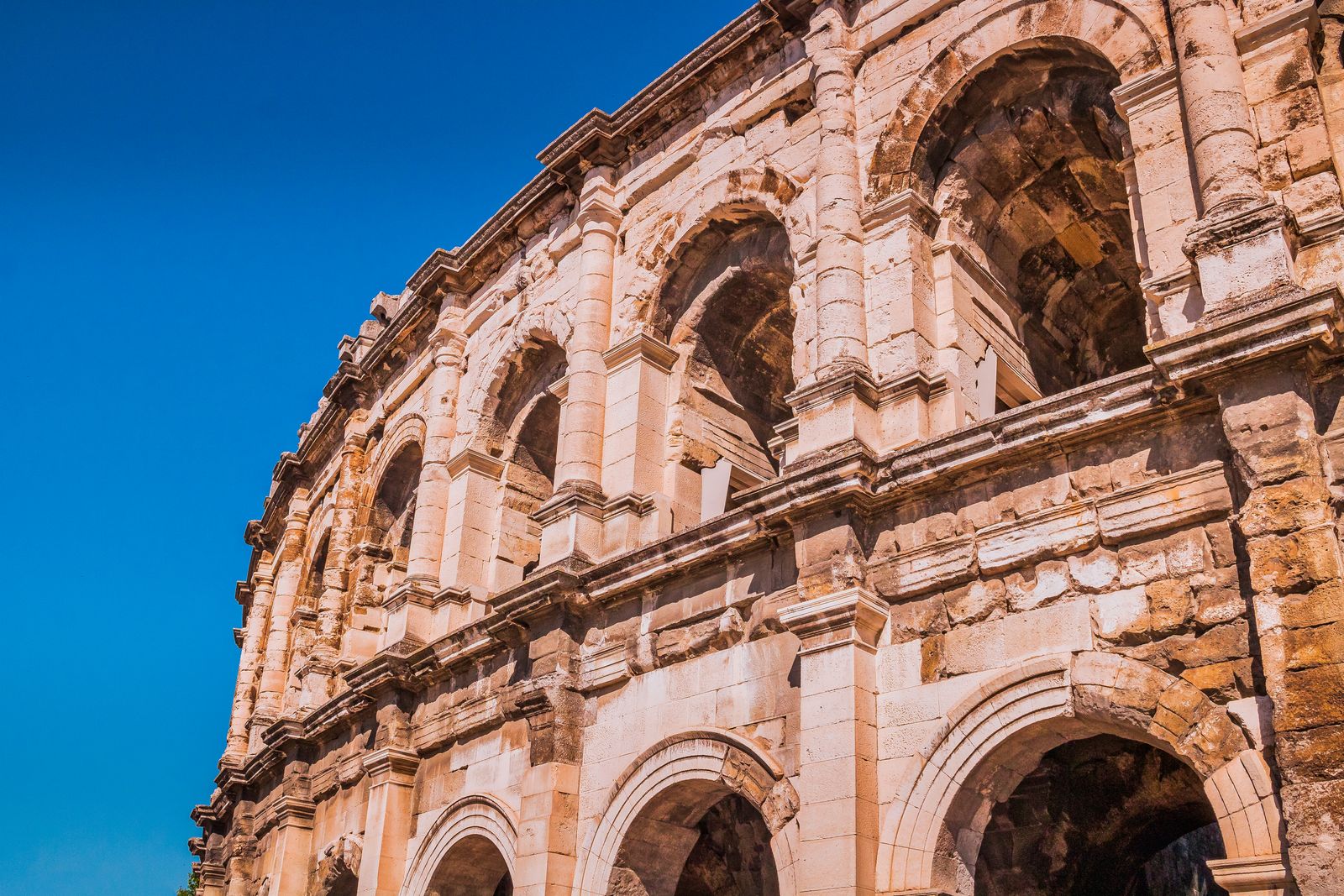La façade en arcades des arènes romaines de Nîmes sous un ciel bleu